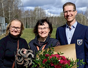 Kolme ihmistä seisoo rinnakkaain keväisessä auringossa.